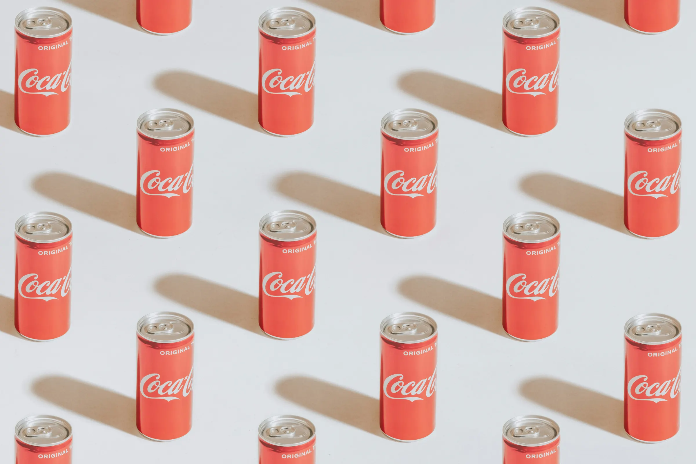 A grid of Coca-Cola cans arranged on a pale background