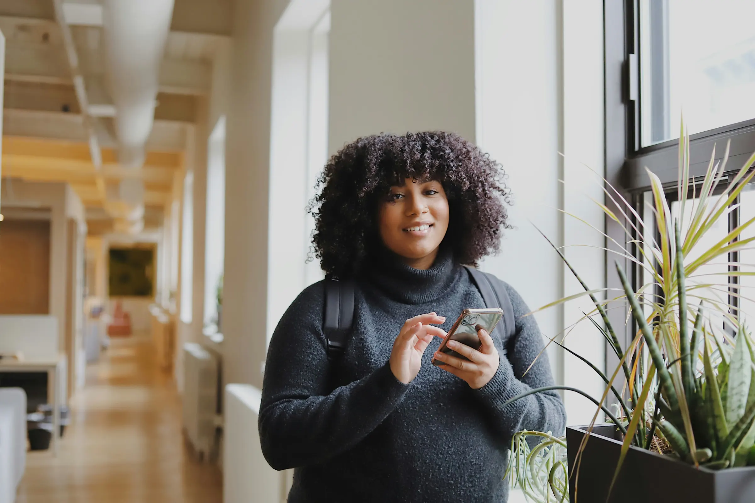 A woman checking her phone in a bright office corridor