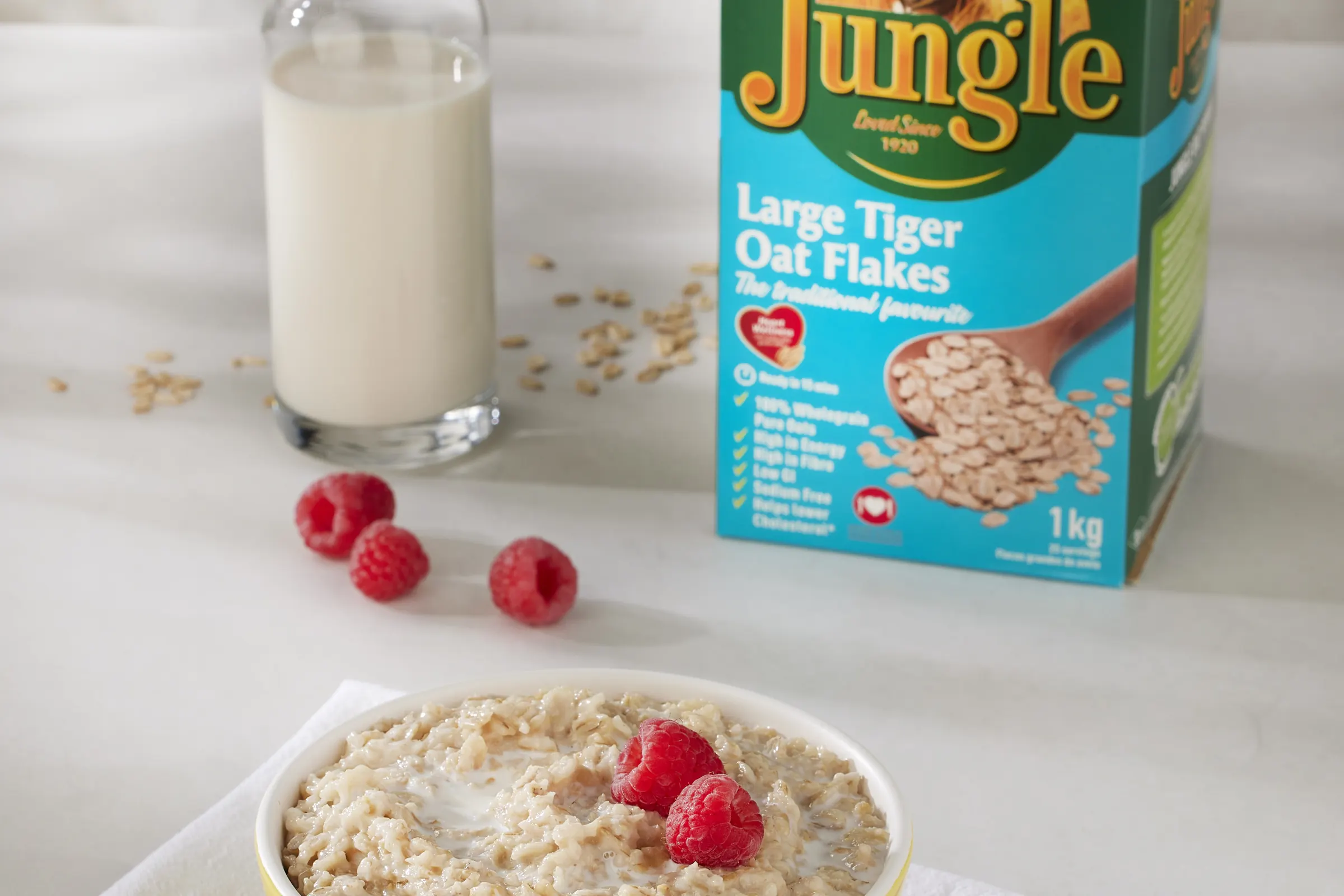 A bowl of Jungle Oats with raspberries, beside the Large Tiger Oat Flakes box